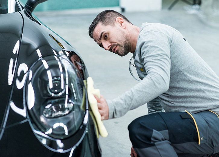 Lackierer poliert schwarzes Auto mit Lappen